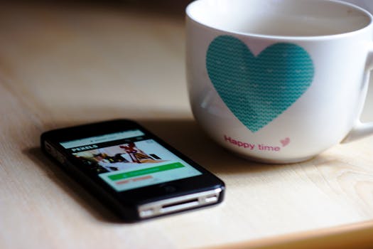 Cozy scene with a smartphone and a heart-decorated coffee mug on a wooden table.