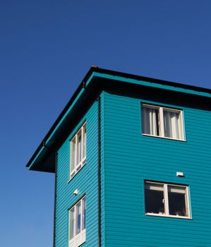 Bright turquoise building corner against a clear blue sky, simple architectural design.