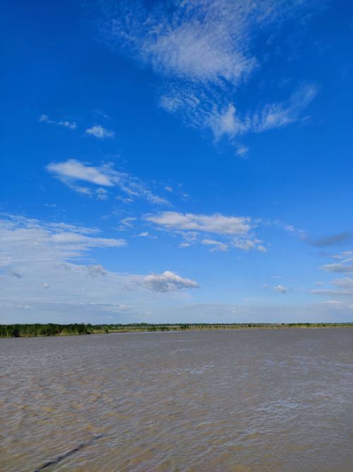 Free Tranquil river scene with expansive blue sky and fluffy clouds, perfect for serene nature themes. Stock Photo
