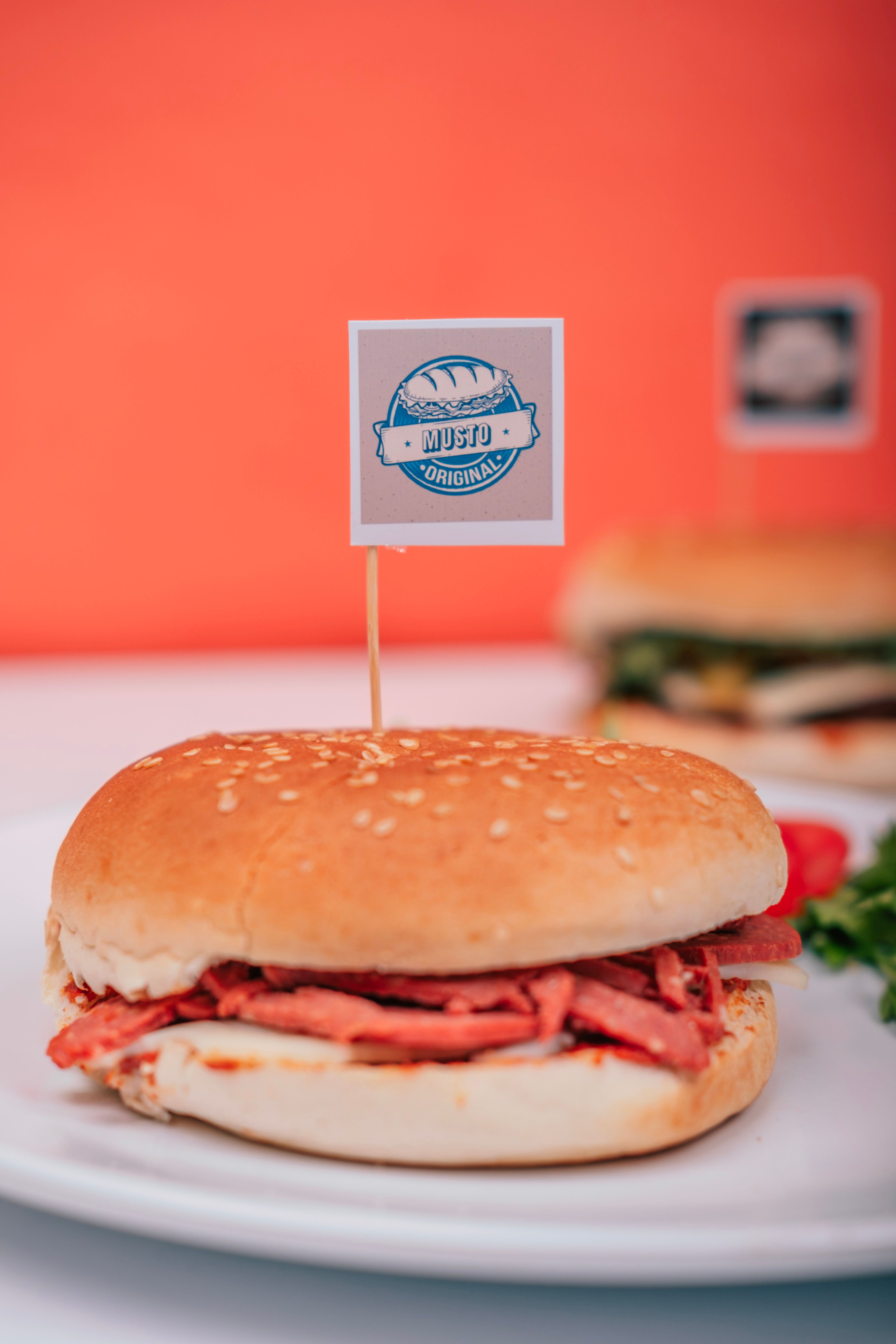 Close-up of a ham sandwich with flag on a white plate, vibrant background.