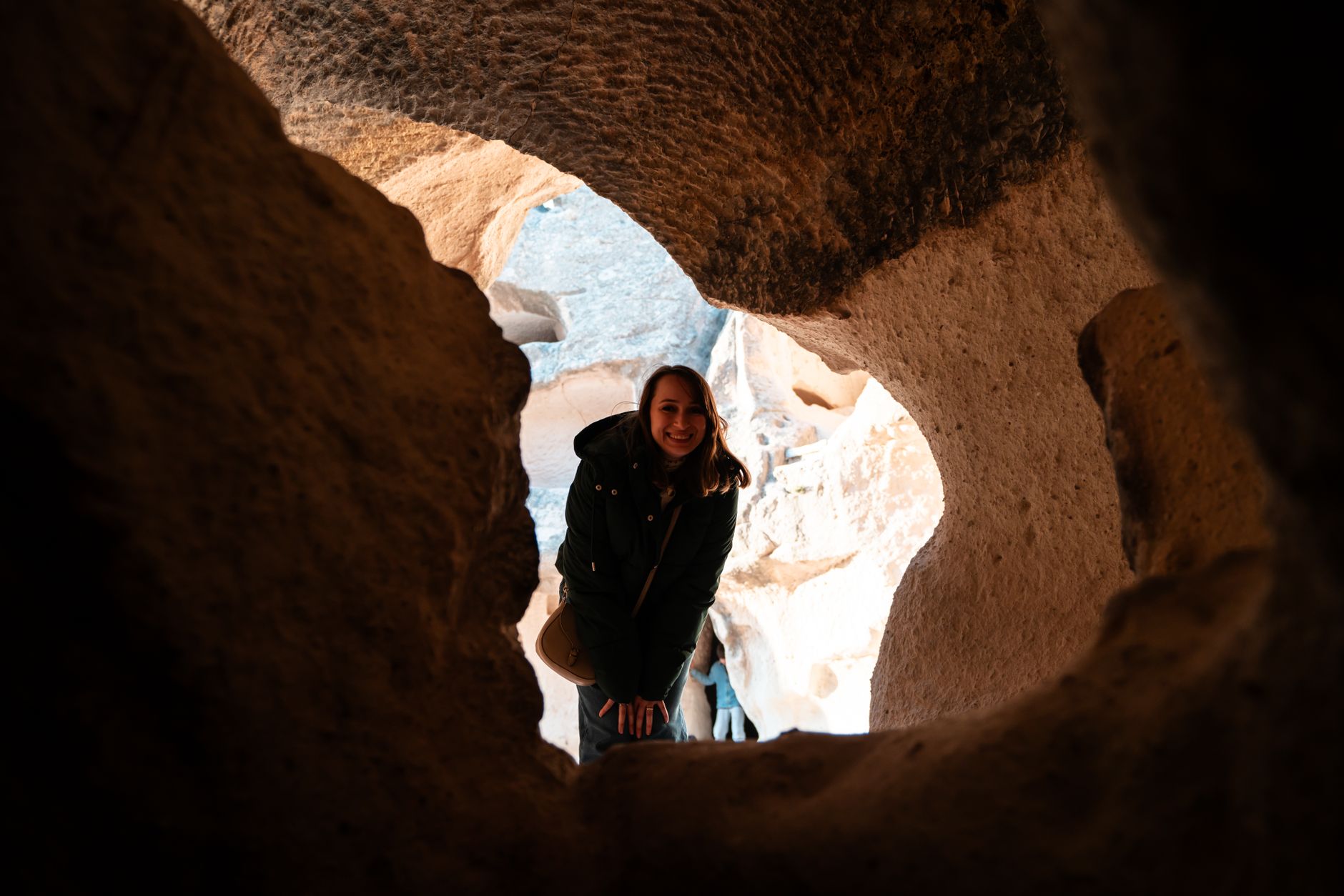 A woman smiling as she explores unique rock formations inside a cave, creating an adventurous and mysterious setting.