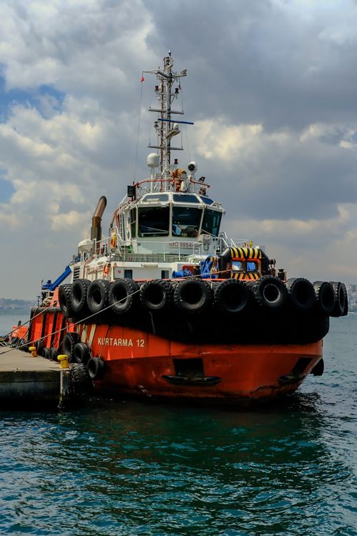 Free A red tugboat docked at a harbor in İstanbul, Türkiye, with a cloudy sky backdrop. Stock Photo