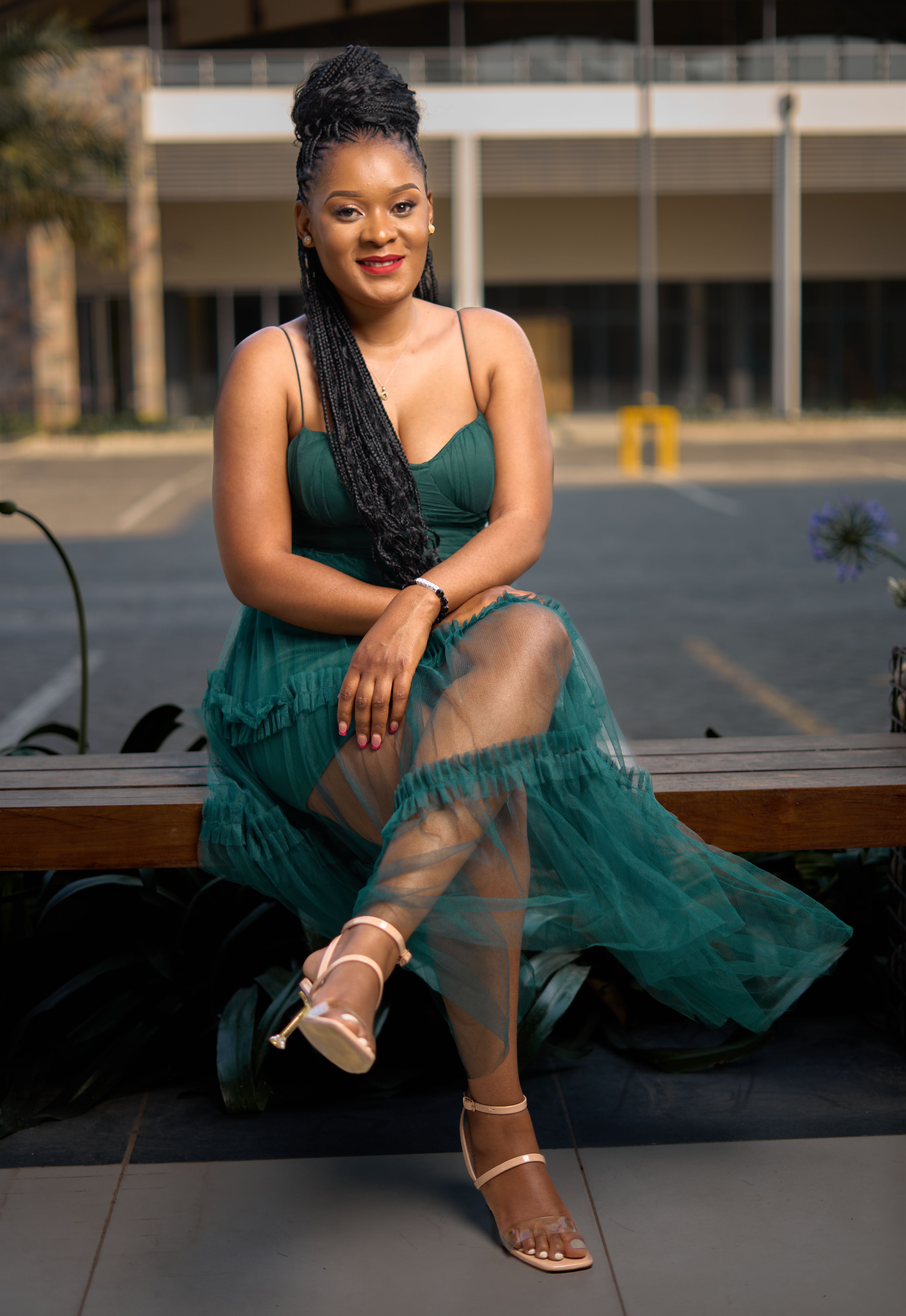A smiling woman elegantly seated on a bench in Lusaka, Zambia, wearing a stylish green dress.