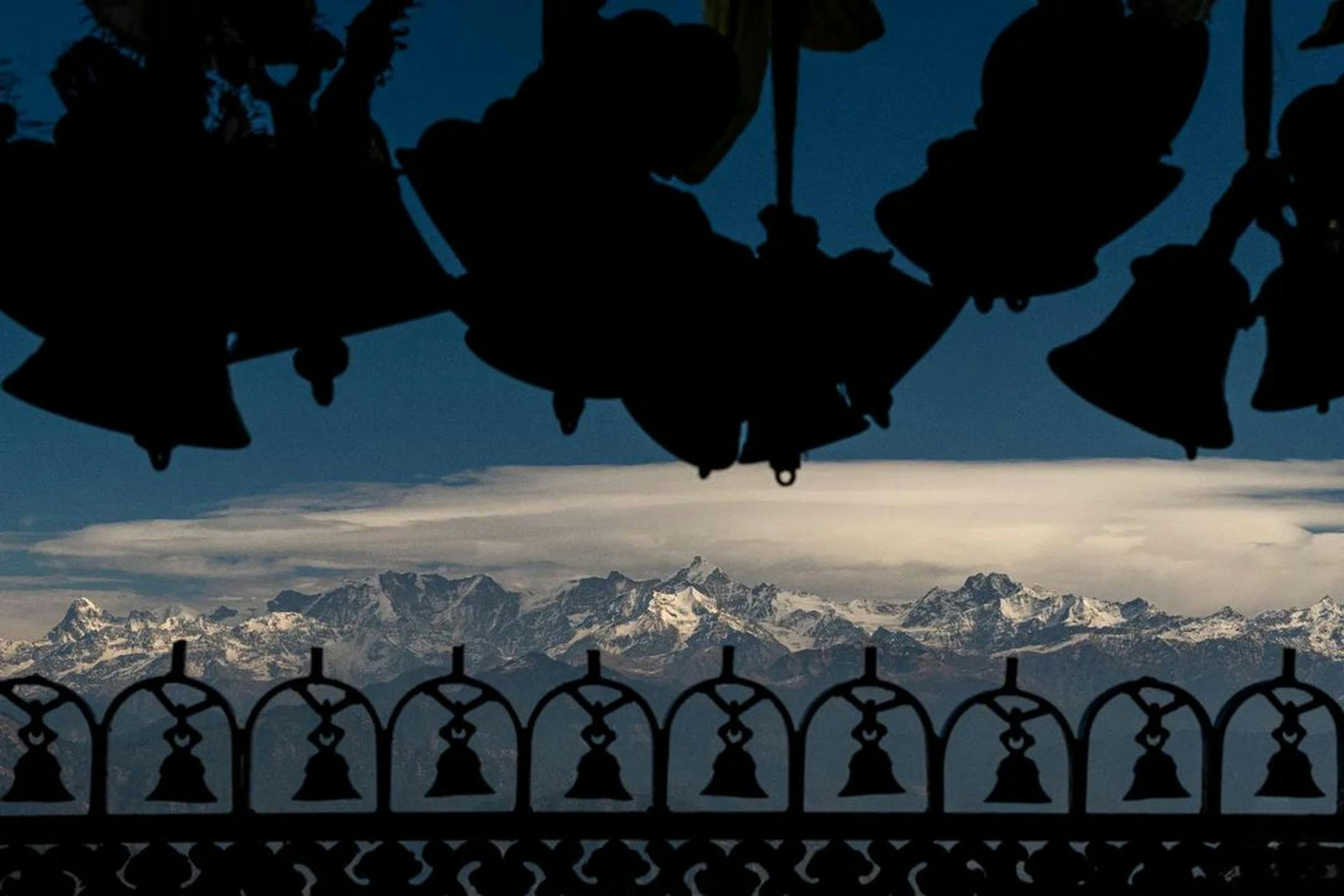 Silhouette of bells framing the majestic Himalayan mountains under a clear sky.