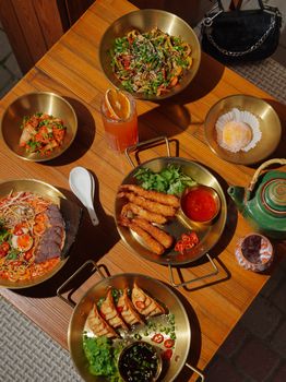 Top view of a diverse Asian meal set on a wooden table with various dishes and tea.