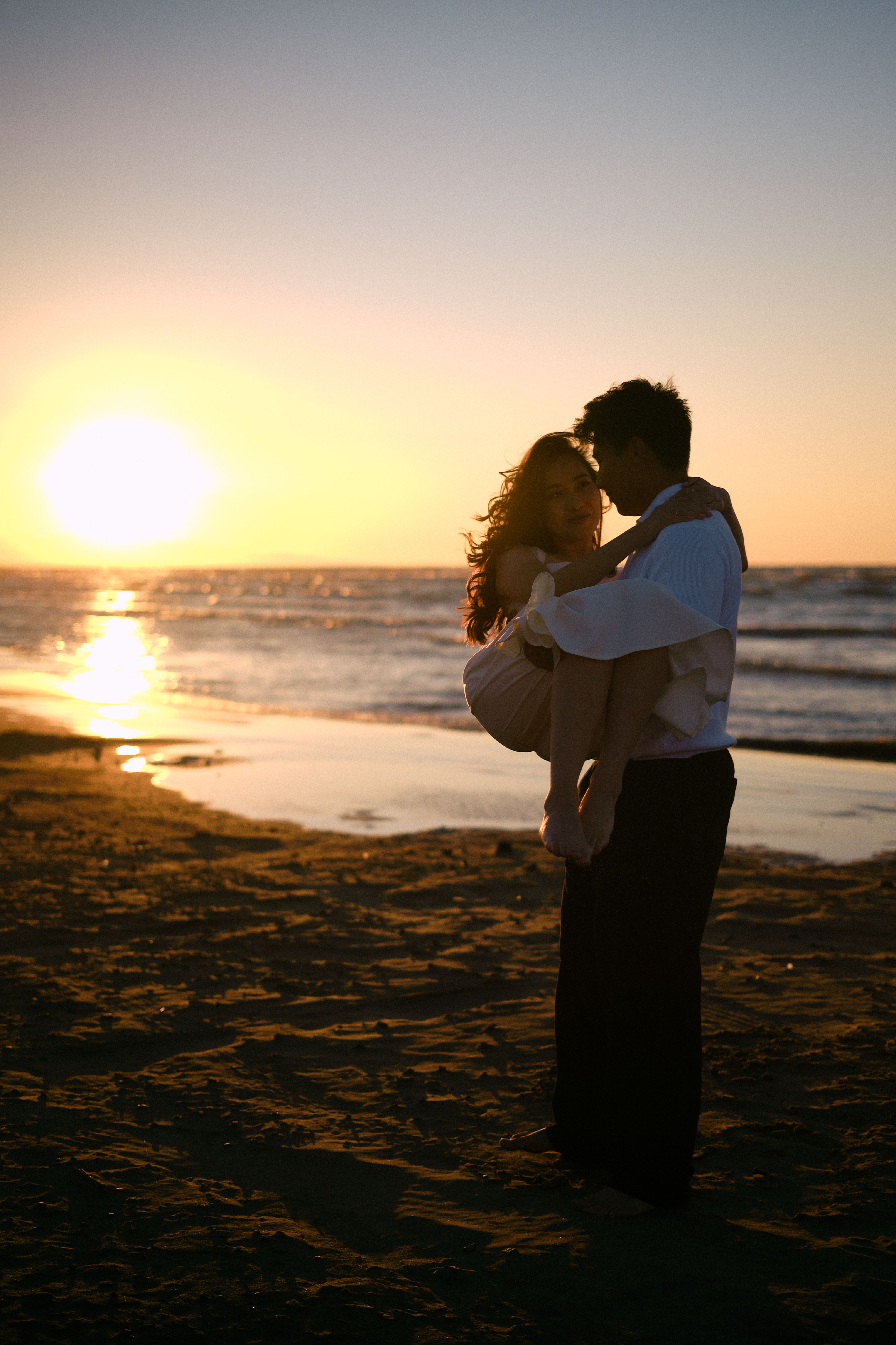 Silhouette of a couple embracing by the beach at sunset, capturing romantic seaside moments.