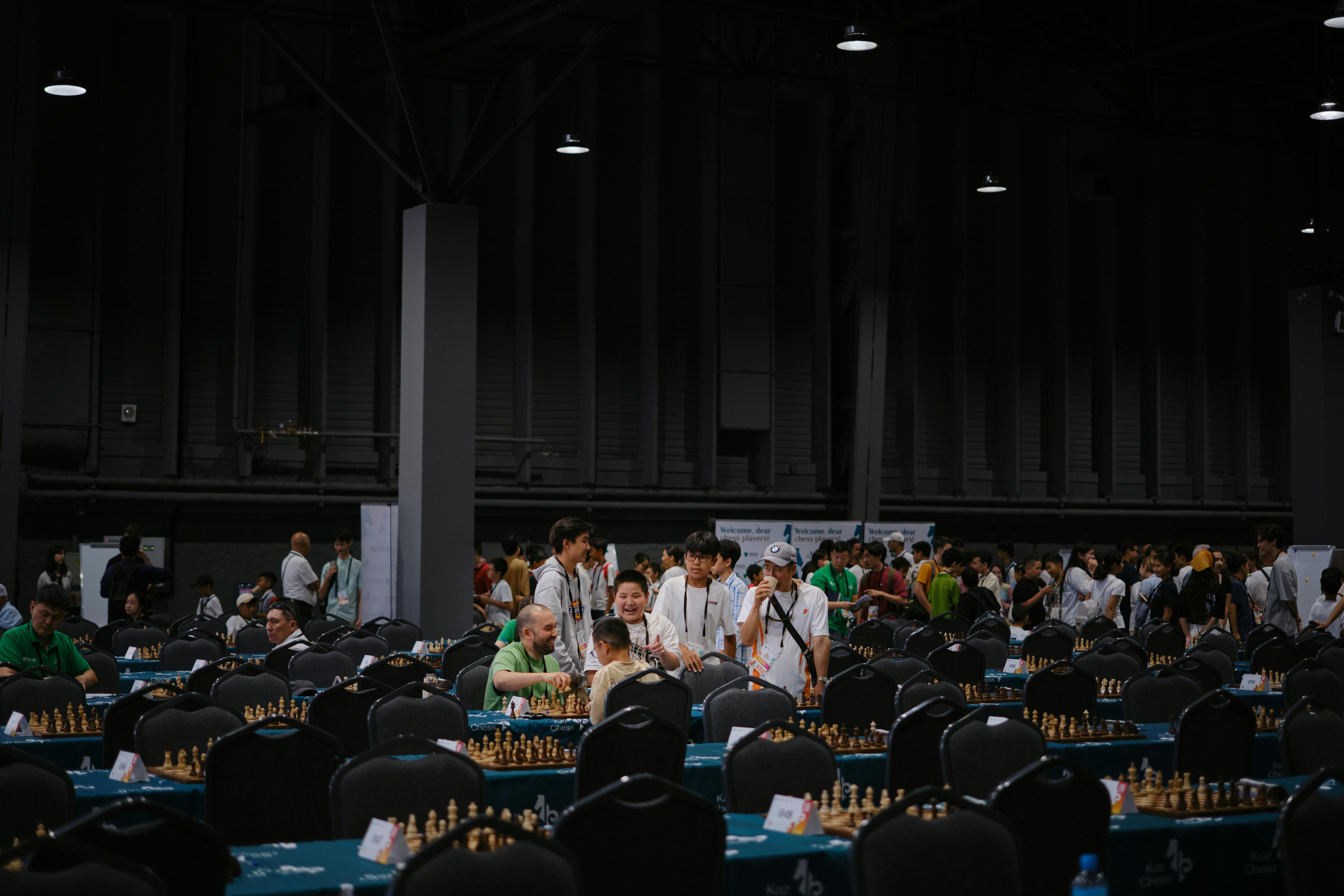 Indoor chess tournament with diverse participants gathering around tables.