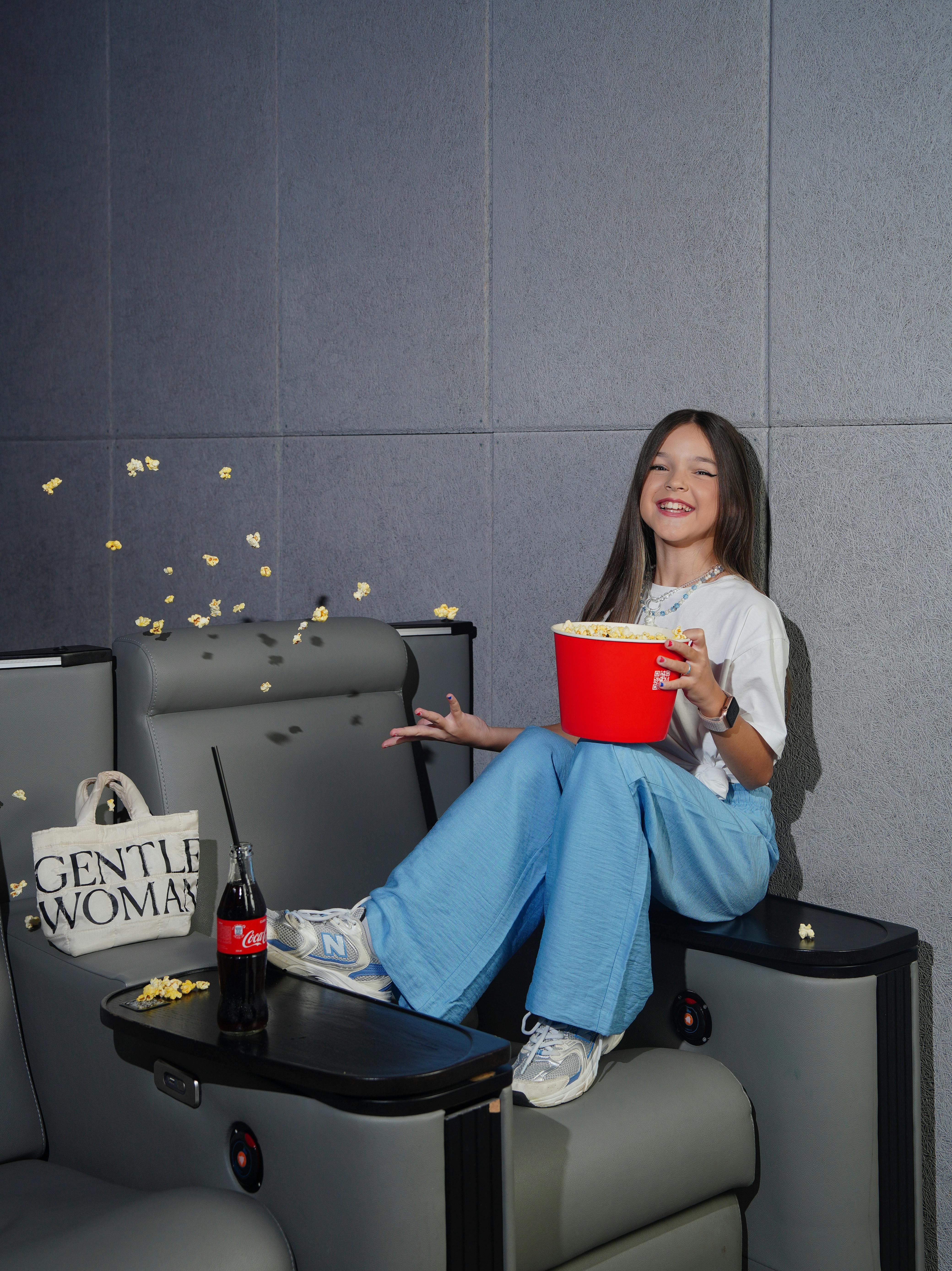 Young girl in leisurewear enjoying popcorn in a stylish home cinema setting.