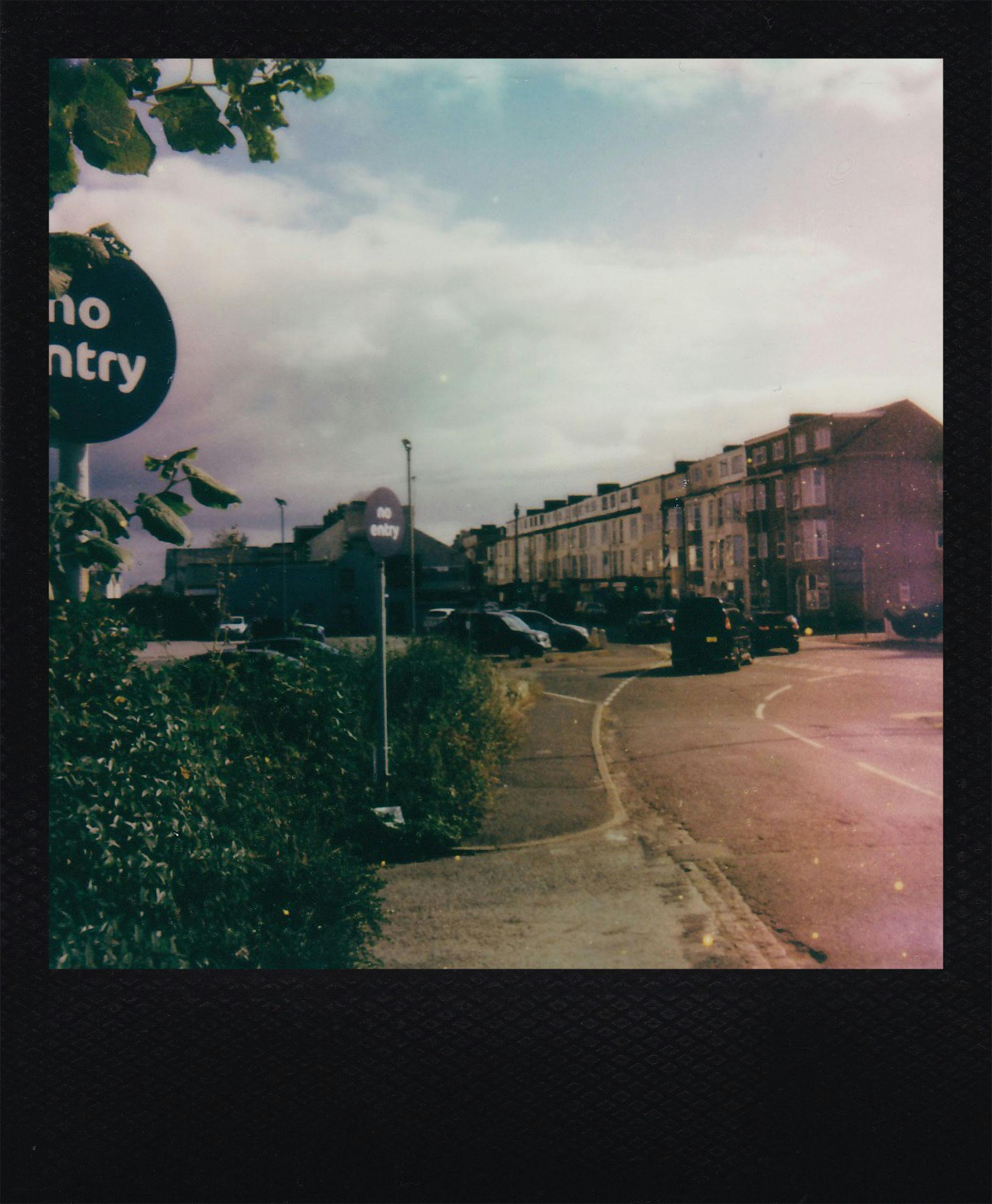 Polaroid of a street with a 'No Entry' sign and vintage buildings.