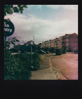 Polaroid of a street with a 'No Entry' sign and vintage buildings.