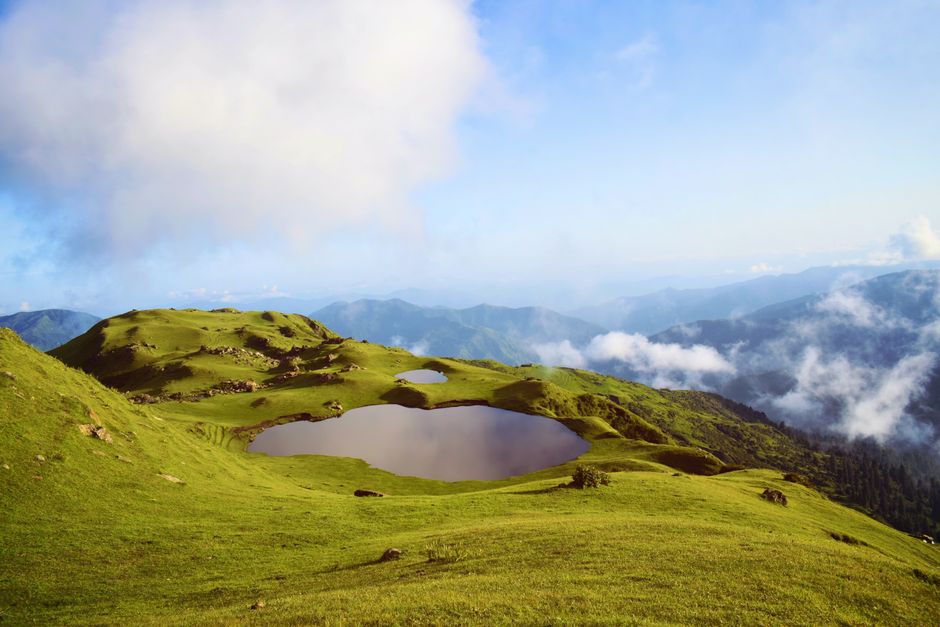 Breathtaking view of lush green hills with a tranquil lake under a vibrant sky in Rawalakot.