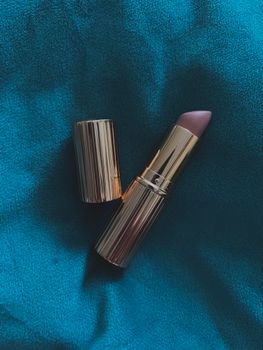 Elegant lipstick displayed against a soft teal fabric background, evoking luxury.