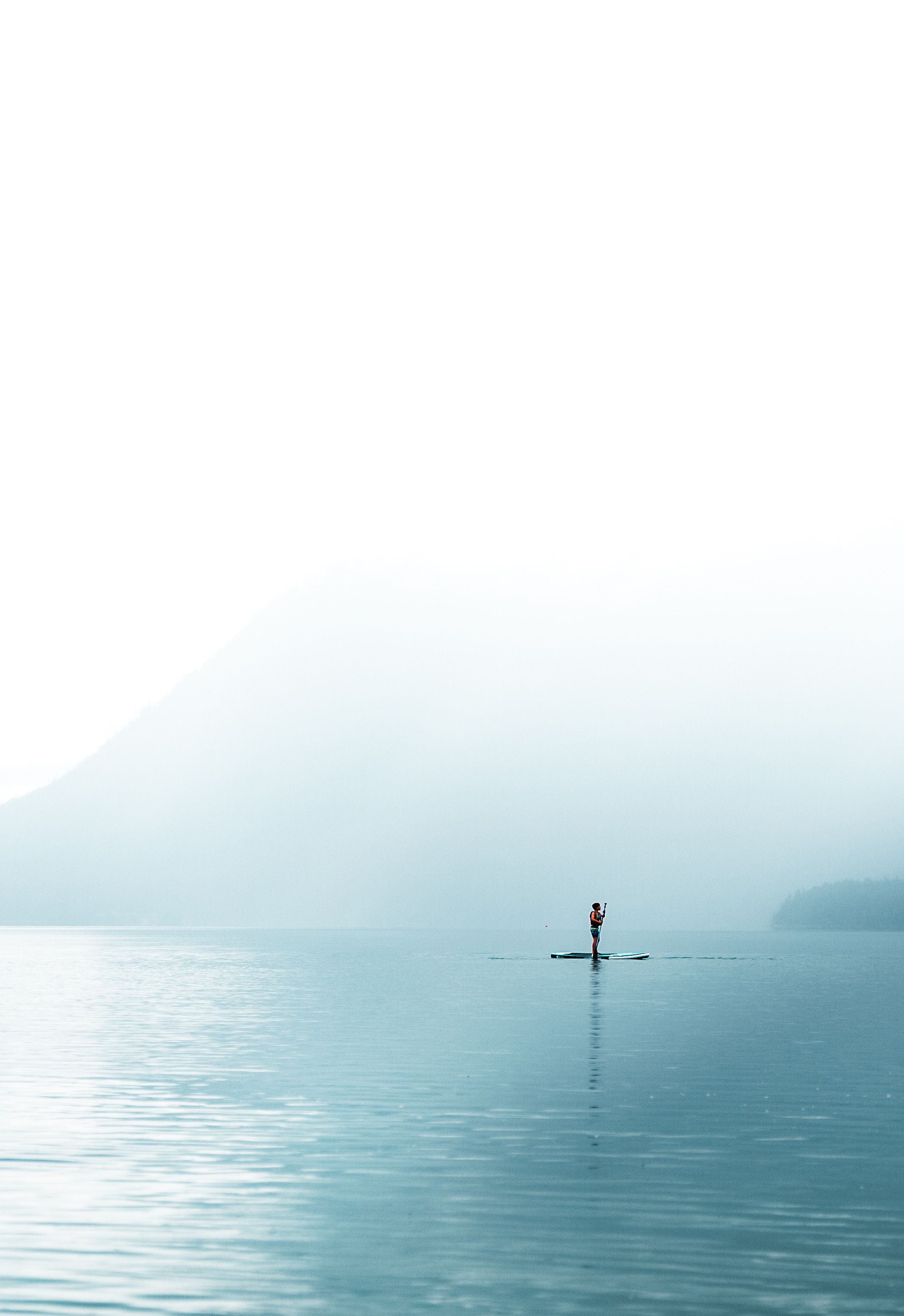 A solitary paddleboarder glides on the calm waters of Kochel Lake, Bavaria, amidst morning mist and mountain scenery.