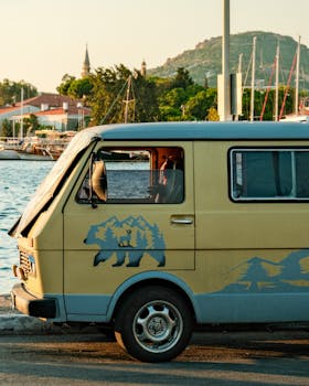 Vintage van parked by a picturesque harbor at sunset, perfect for travel and adventure themes.