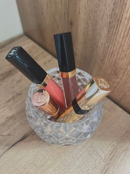 Four luxury lipsticks in a crystal holder on a wooden surface.