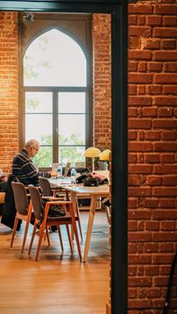 Casual workspace with exposed brick walls and large window, featuring a senior adult using a laptop.