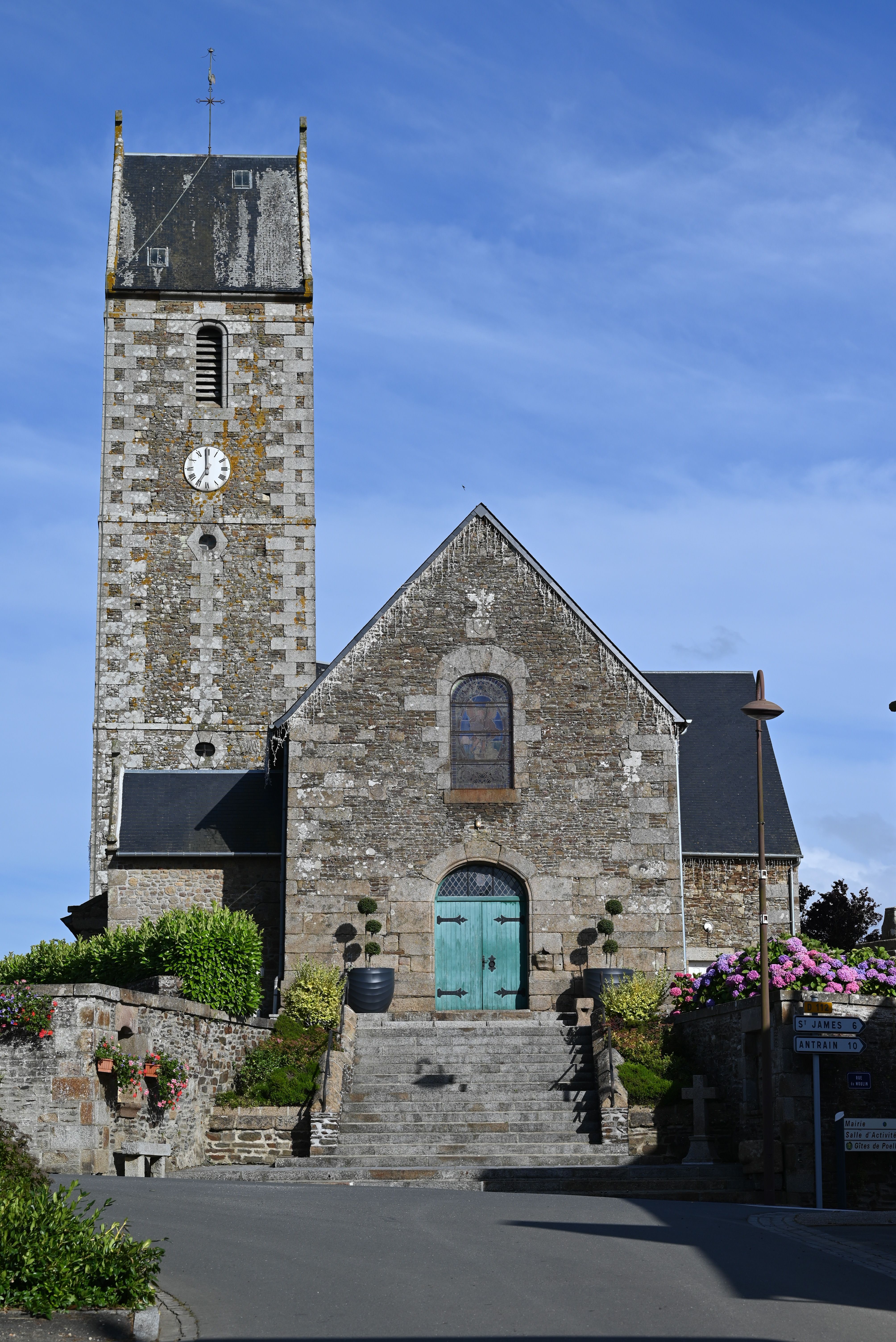 Charming stone church with clock tower, light blue sky, and blooming flowers.