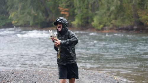 Free Boy celebrates catching a fish on a rainy day by the riverbank. Stock Photo