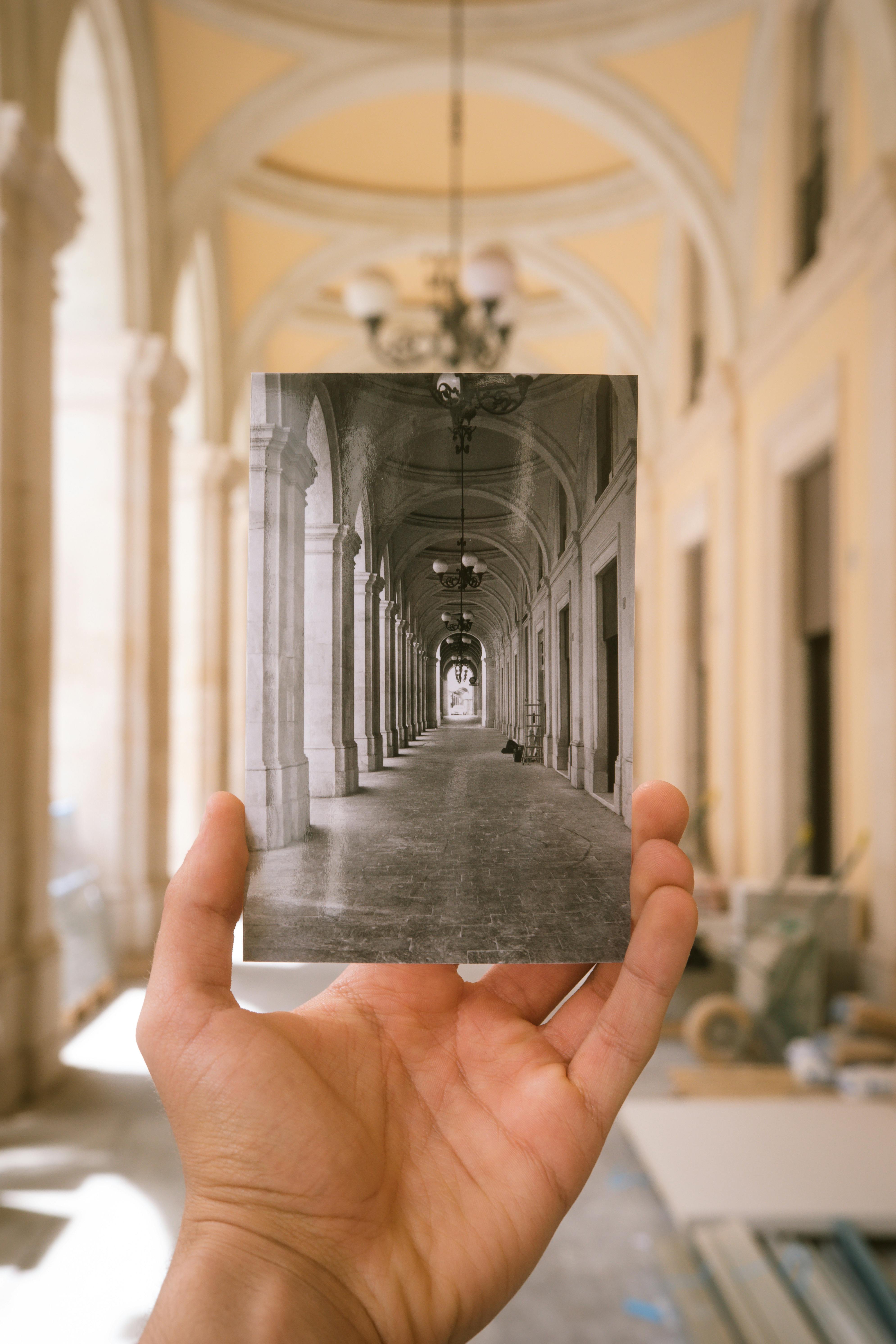A hand holds a vintage photo in a grand architectural hallway.