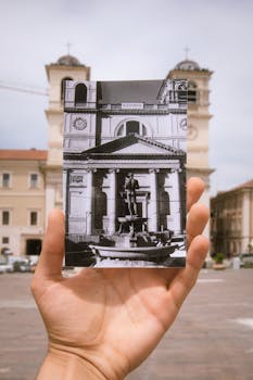A hand holding a historic photo in an Italian city square.