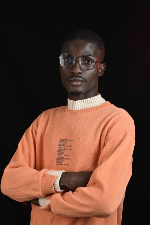 Free Confident young man in an orange sweater and glasses posing against a black background. Stock Photo