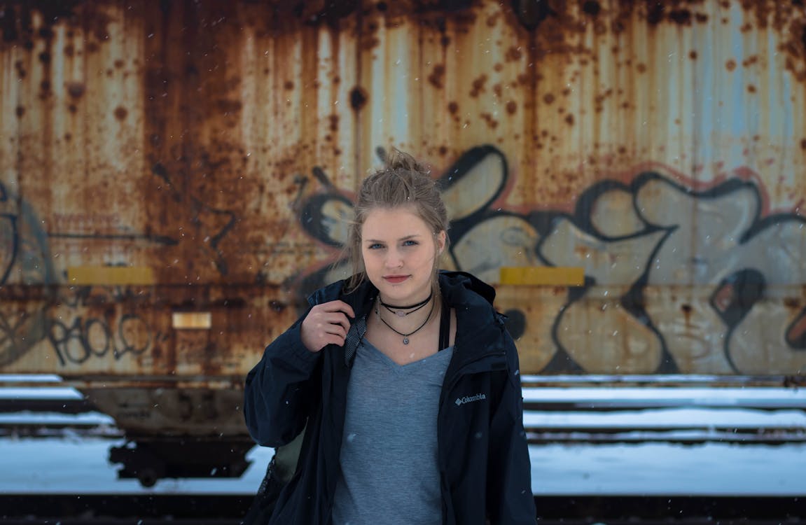 Woman Wearing Black Jacket Standing in Front of Brown Mural