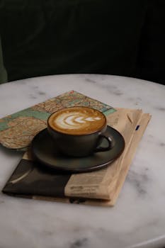 A cup of latte with latte art sits on a newspaper and a map, creating a cozy coffee scene.
