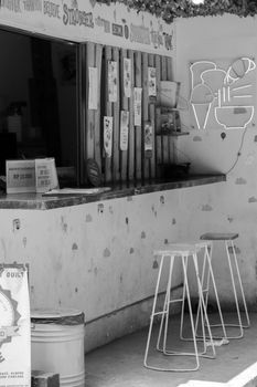 Monochrome image of a street cafe counter with stools under a bright sign.