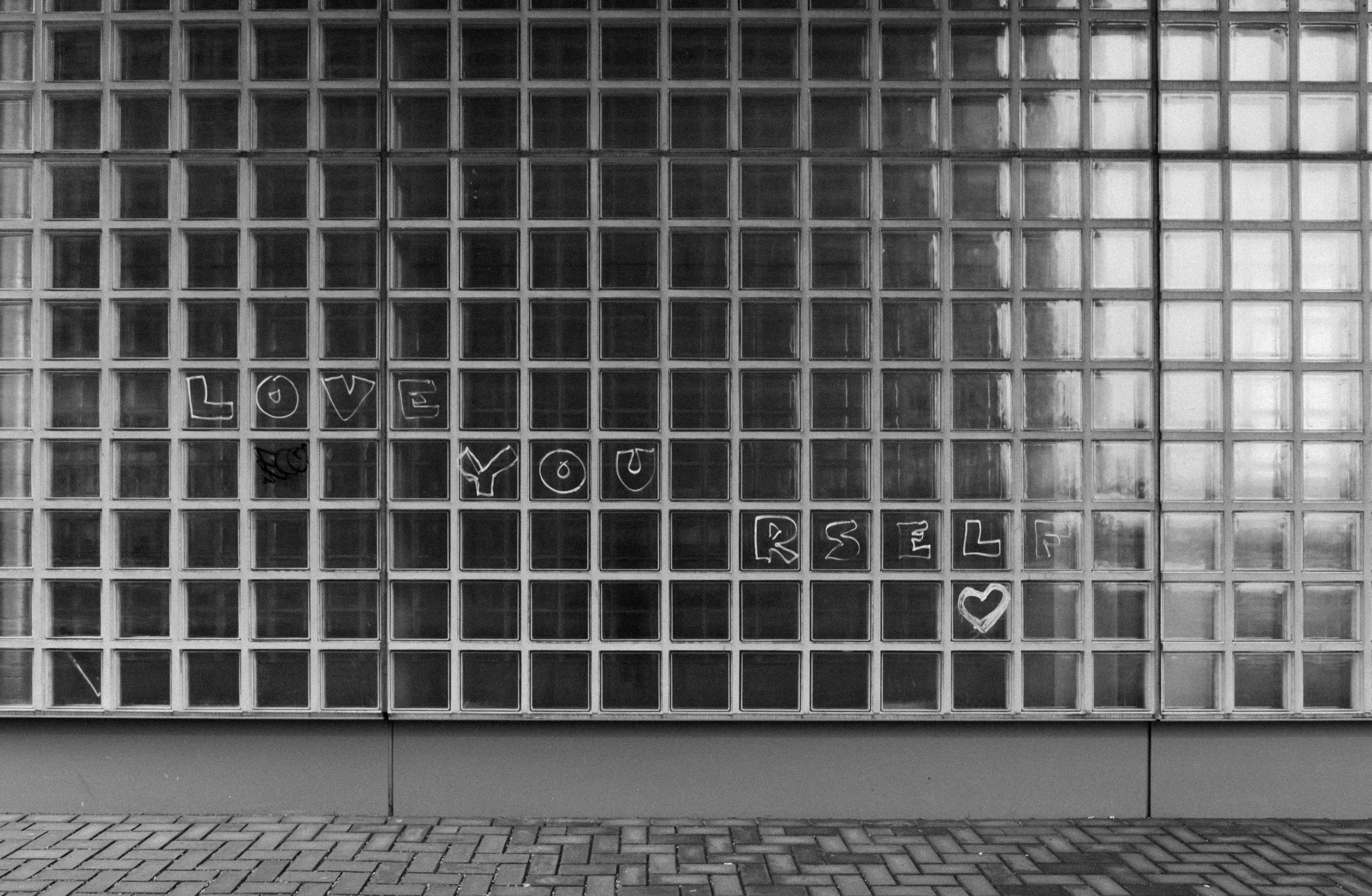 Black and white photo of a glass wall in Amsterdam with the 'Love Yourself' quote.