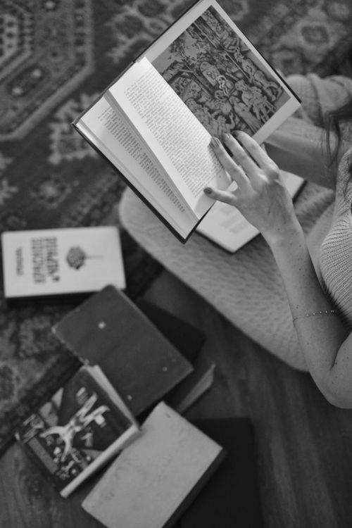 Free Black and white image of a person reading books on a patterned rug, creating a cozy and vintage ambiance. Stock Photo