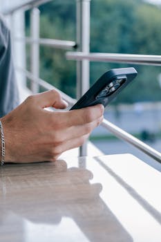 A person's hand holding a smartphone with a blurred outdoor background.