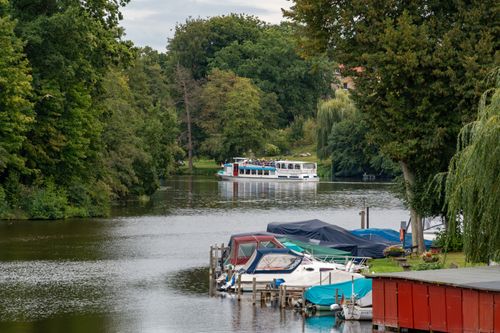 Free Charming river scene with a boat cruising, surrounded by lush greenery. Stock Photo