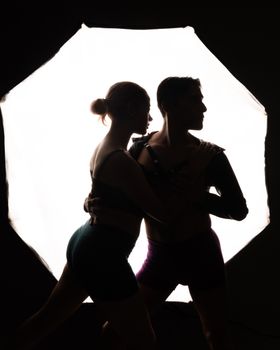 Silhouetted dancers embrace in a backlit scene, capturing an intimate artistic moment.