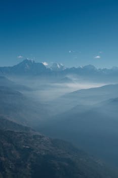 Stunning aerial view of a mountain range with misty valleys and blue sky.