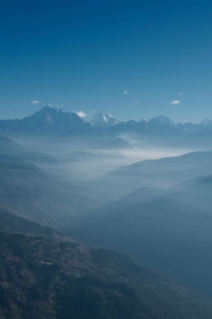 Stunning aerial view of a mountain range with misty valleys and blue sky.