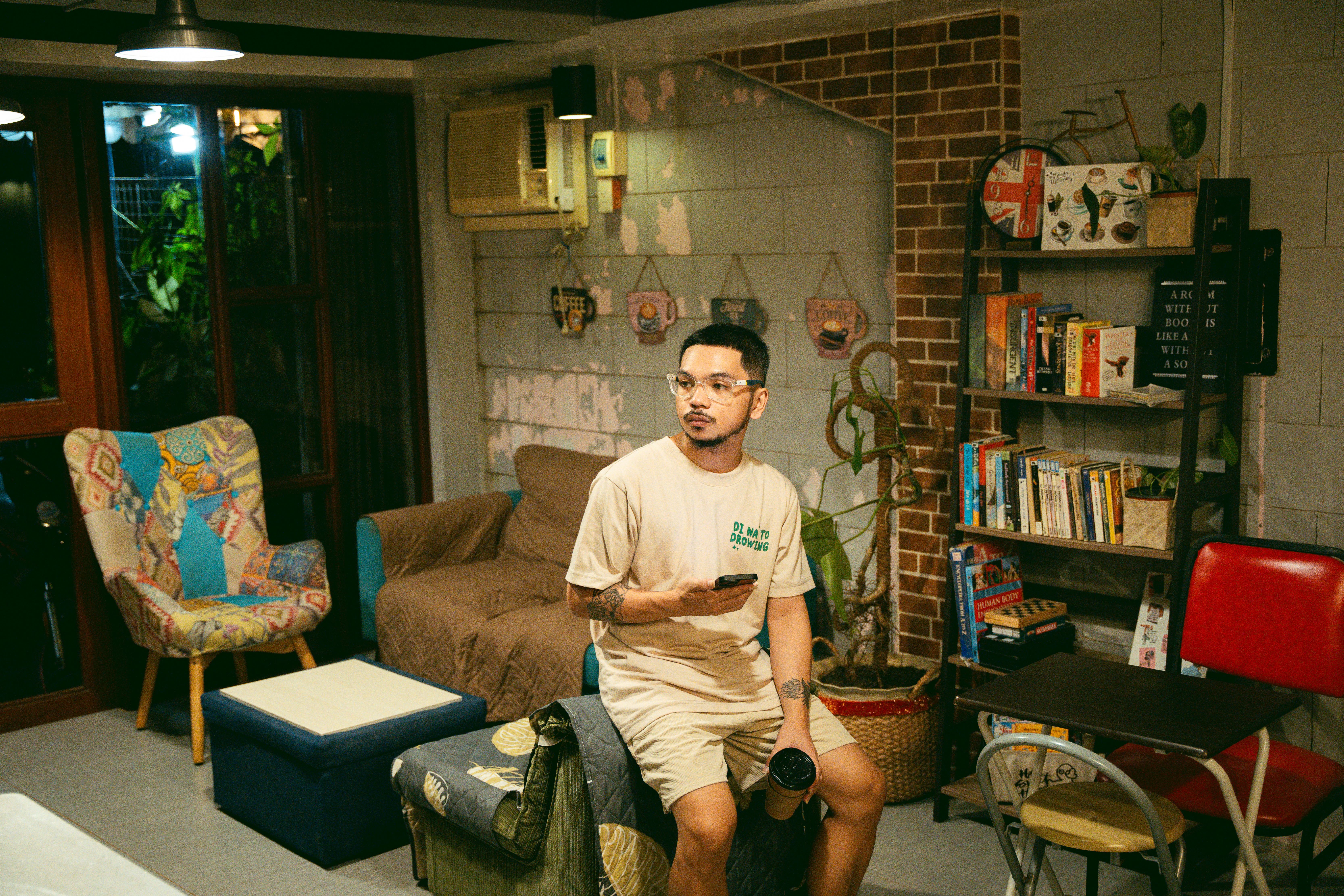 Adult man in a casual setting, surrounded by books and retro decor with a camera.