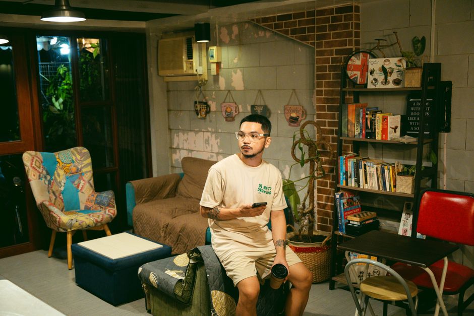 Adult man in a casual setting, surrounded by books and retro decor with a camera.