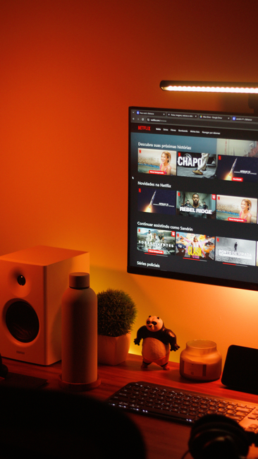 Fotomural Configuración de oficina en casa cálidamente iluminada, con un monitor de ordenador que muestra la interfaz de un servicio de streaming.