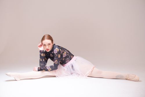 Free Ballet dancer wearing a floral top and tutu, performing a split pose in a studio setting. Stock Photo