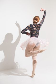 A ballet dancer performing elegantly in a bright studio, casting a shadow on the wall.