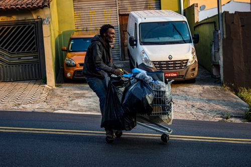 Free Man pushing a shopping cart loaded with bags in an urban environment, depicting daily life and resilience. Stock Photo