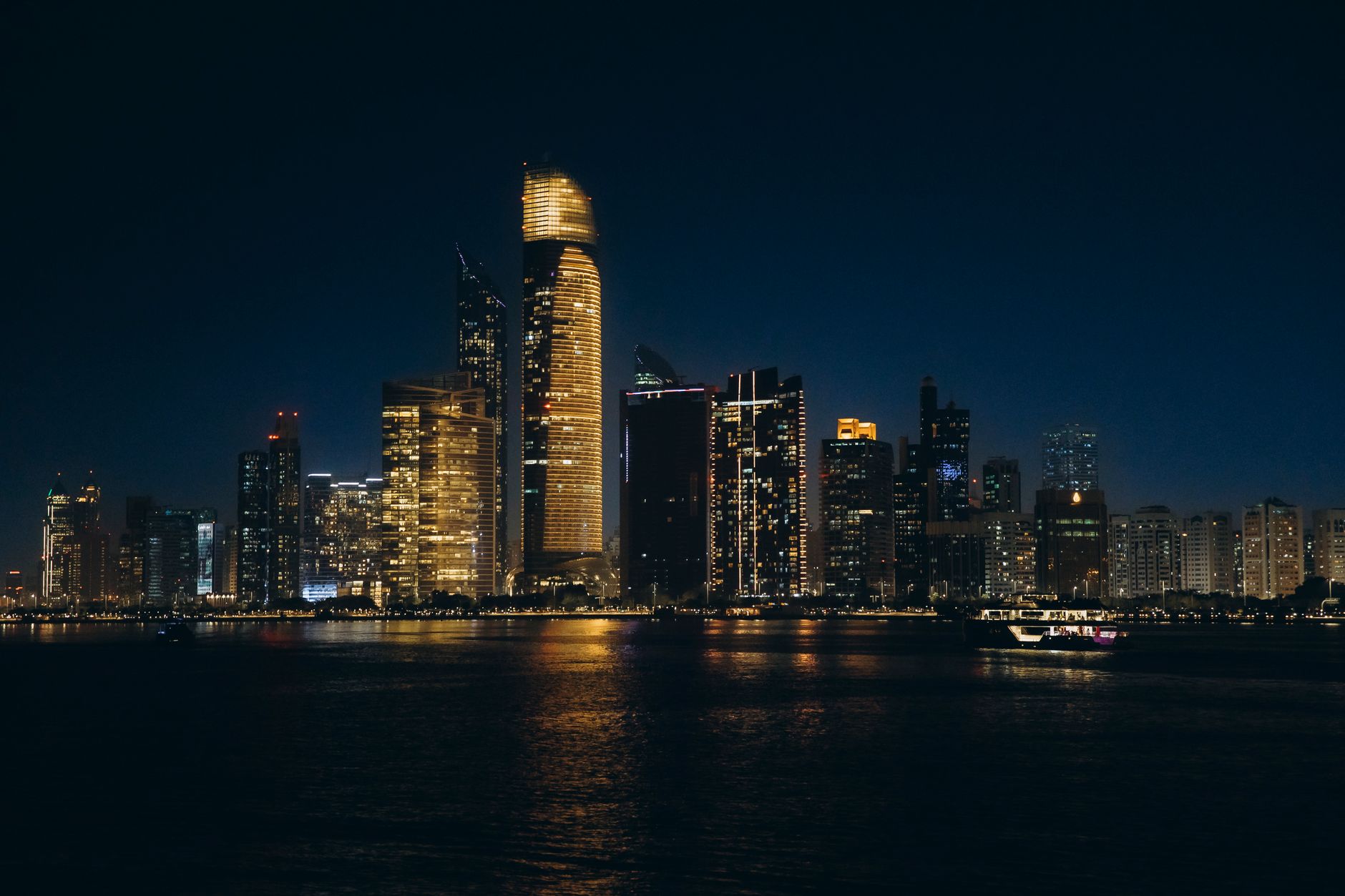 Stunning night view of Abu Dhabi skyline with illuminated skyscrapers reflecting on water.