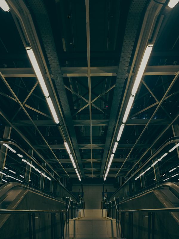 Vista de uma moderna escada rolante de metrô com iluminação industrial e design arquitetônico.