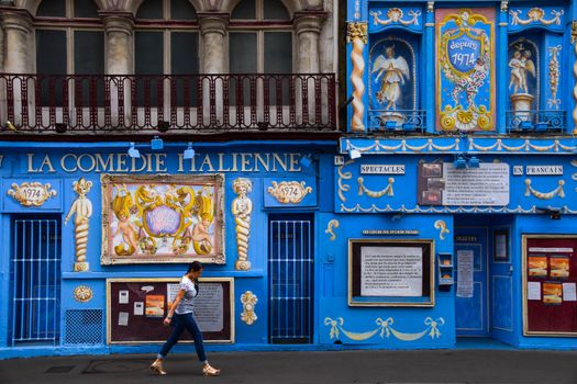 Vibrant blue facade of La Comedie Italienne theater with a passerby in Paris, France.
