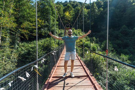 A man enjoying a sunny day on a suspension bridge surrounded by lush greenery in Gagra.