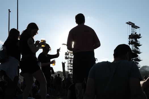 Silhouetted crowd enjoying a music festival with bright sun, capturing the lively atmosphere.