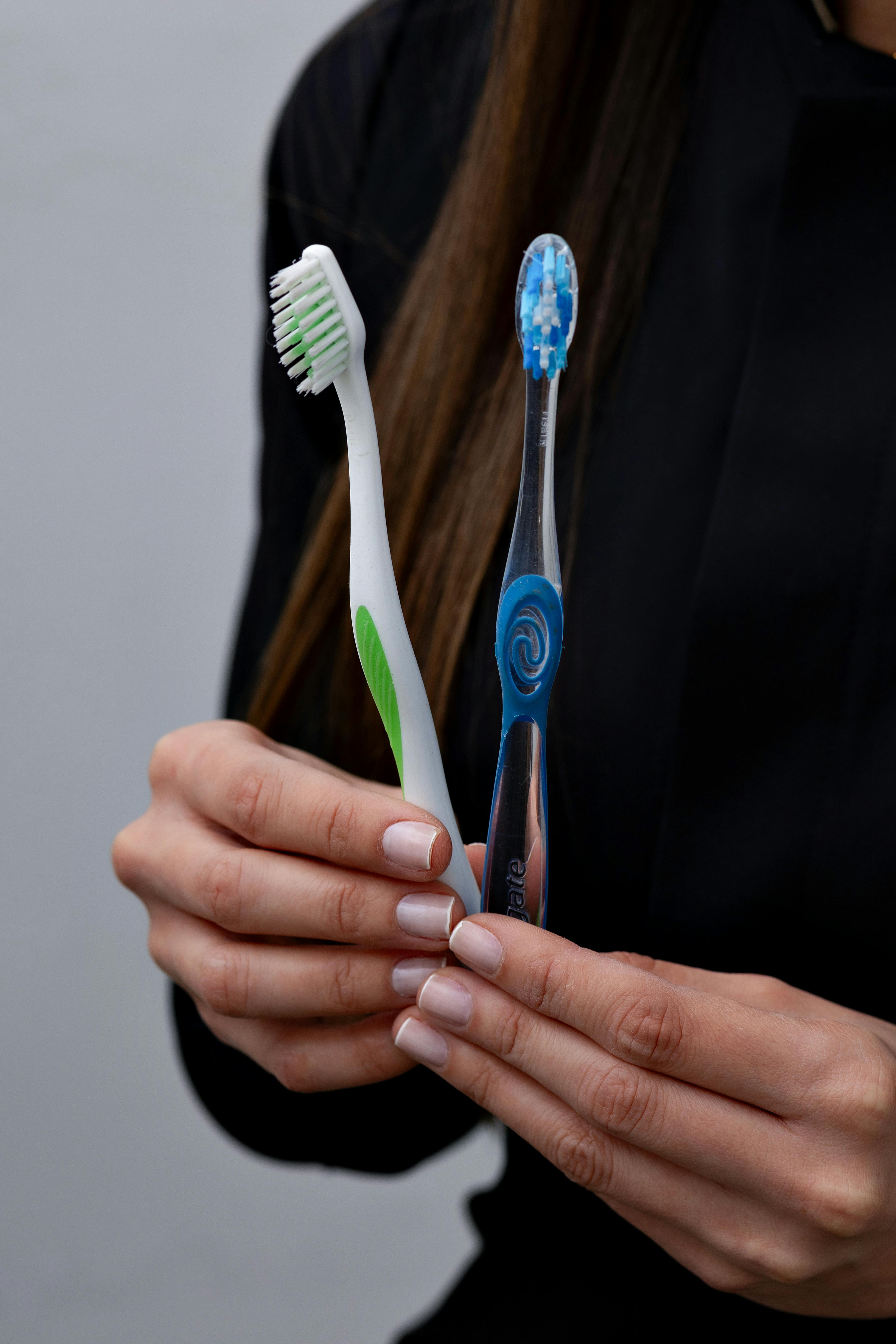 Close-up of hands holding two toothbrushes in a dental care setting.
