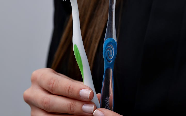 Close-up of hands holding two toothbrushes in a dental care setting.