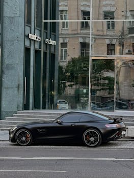Elegant black sports car parked by modern building in Kyiv, Ukraine, reflecting urban style.