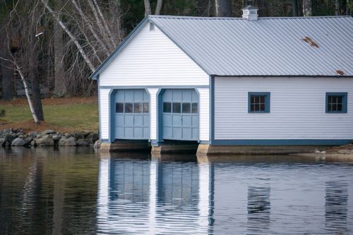 Free A serene boathouse reflecting on a calm lake surrounded by bare trees. Stock Photo